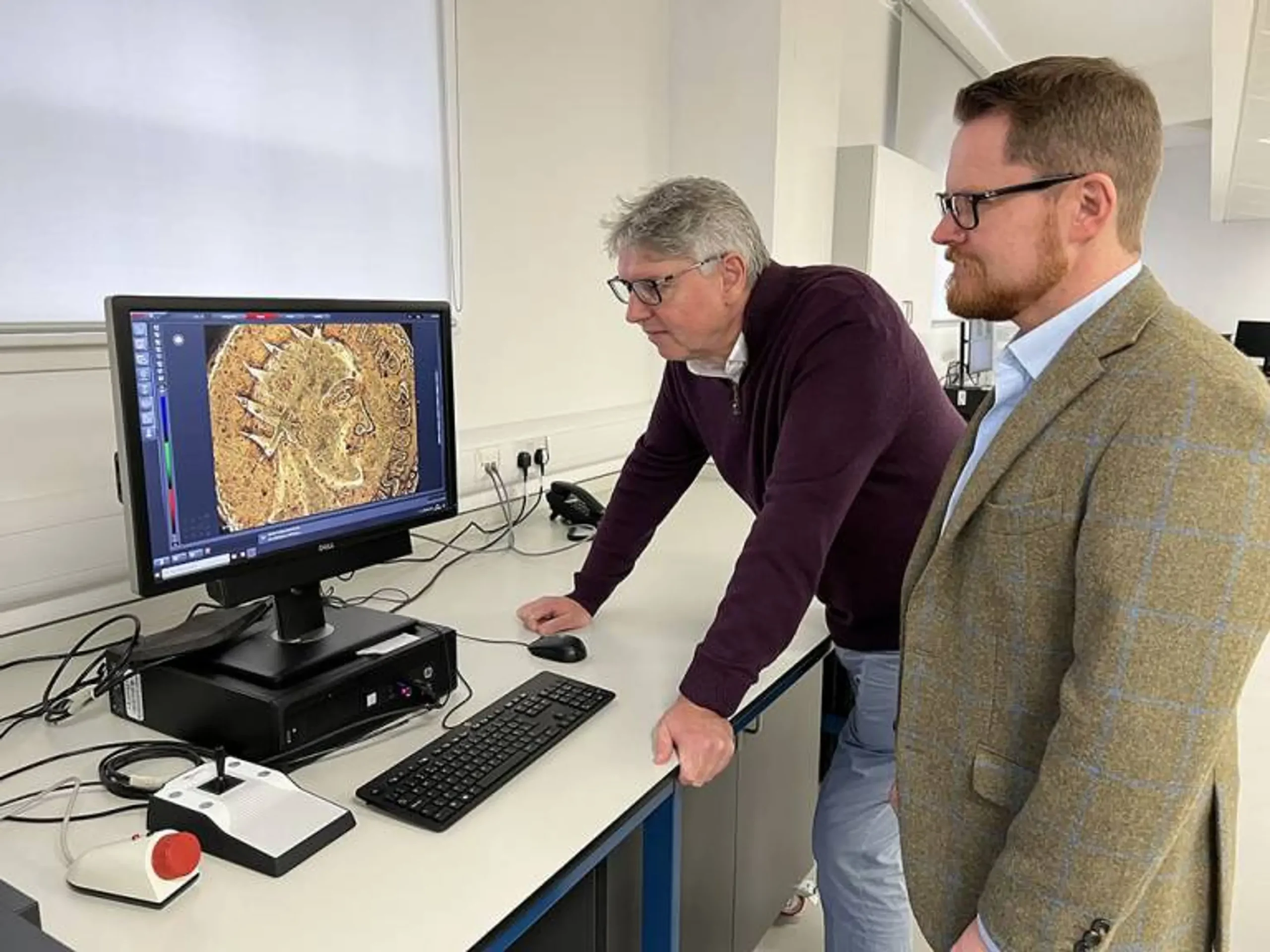保罗-N-皮尔森教授和杰斯珀-埃里克森在强大的显微镜下检查斯邦尼金币 图像来源/格拉斯哥大学亨特里安博物馆
